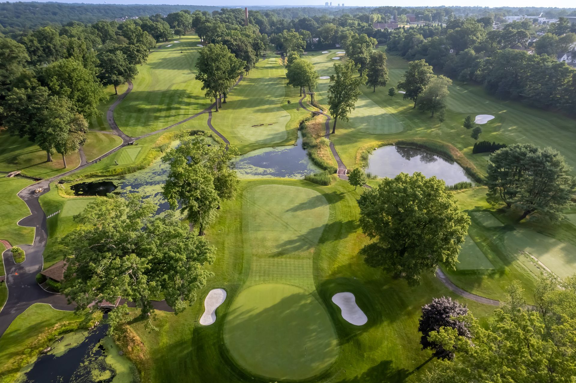 An aerial view of a lush green golf course hole with a sand bunker on each side of the putting green and a pond ahead.