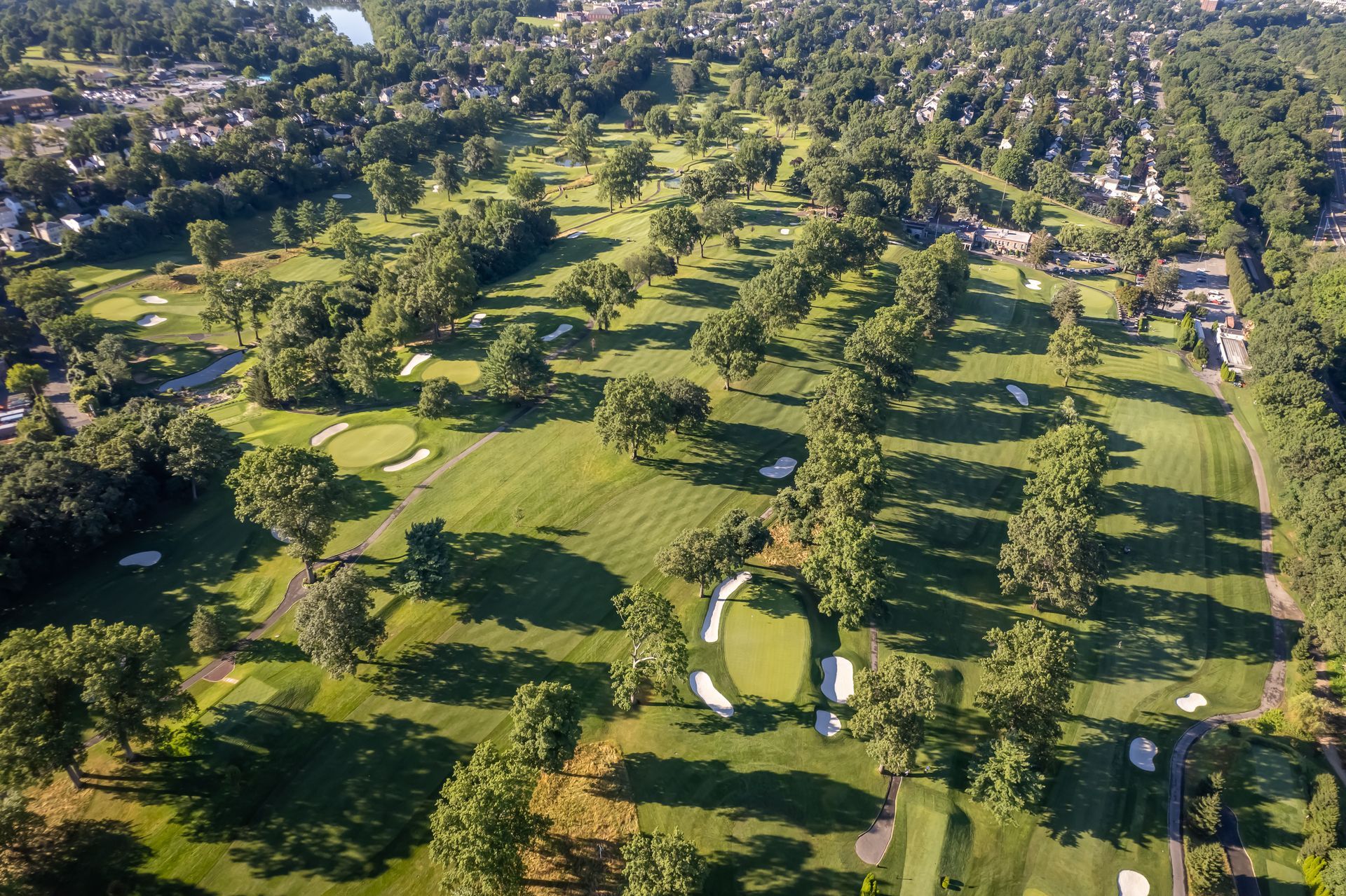 Aerial view of a green golf course with trees, bunkers, and fairways.