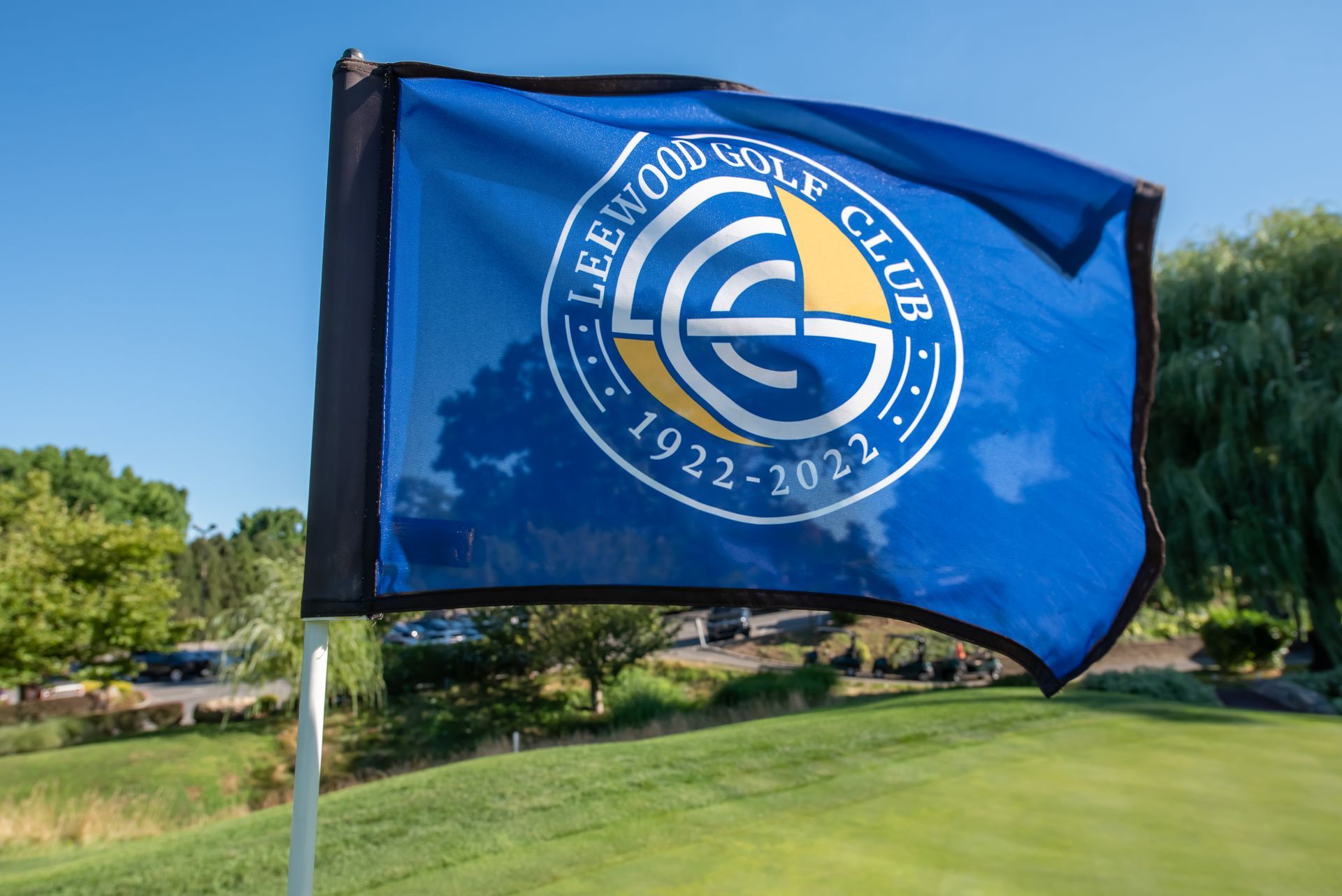 Blue golf flag with the Lee Wood Golf Club logo waving on a green course.