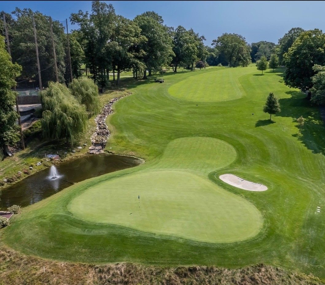 Green golf course with a pond, a sand trap, and trees.