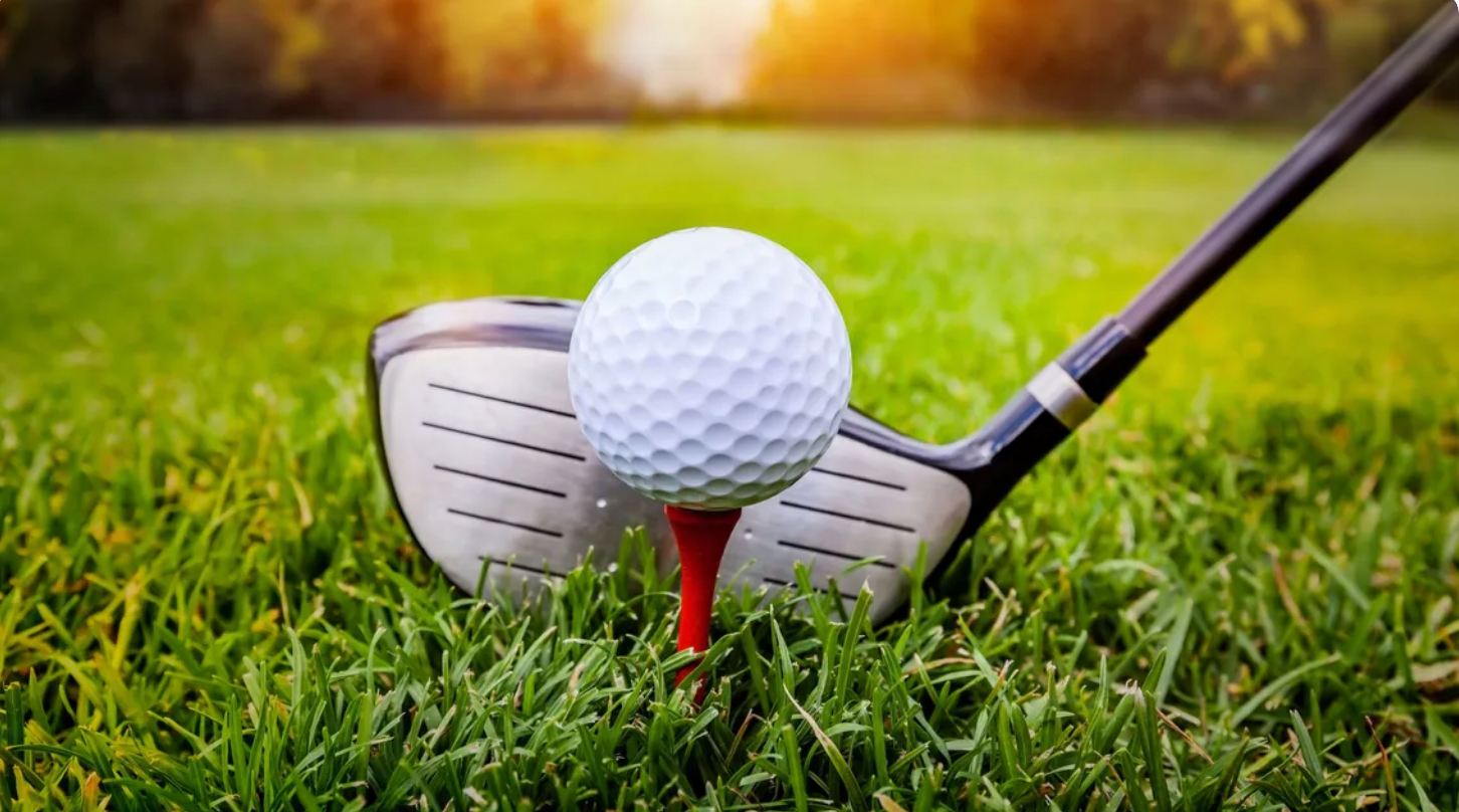 Golf ball on tee ready to be hit with a golf club on green grass.