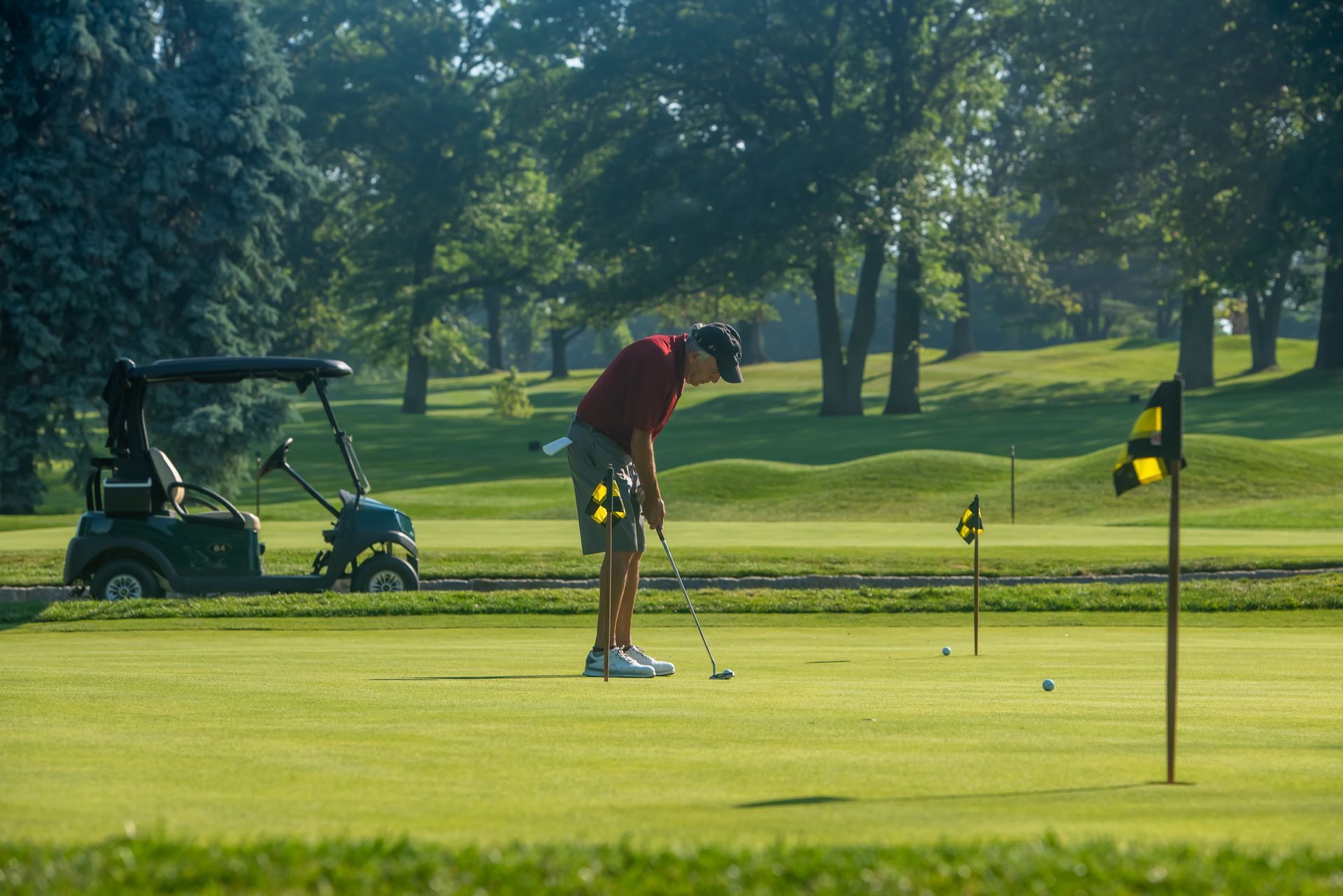 Man coaching a young girl on a golf course, pointing to the ball and stance.