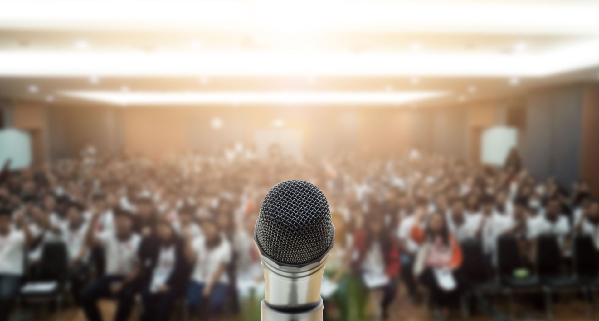 Close-up of a microphone with a blurry audience in the background, likely a presentation or speech event.