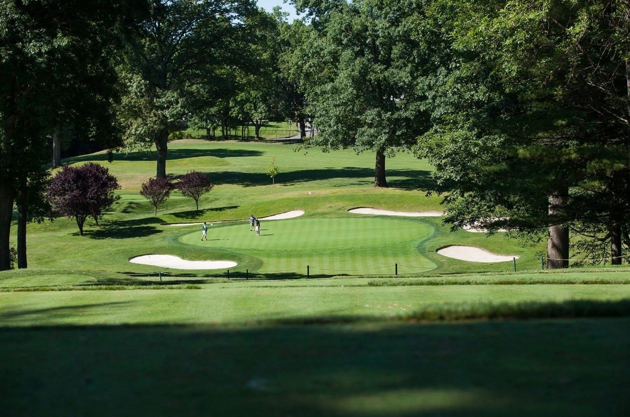 Golf green with sand traps, trees, and players putting.