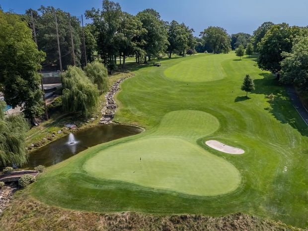 Green golf course with a pond, sand trap, and trees.