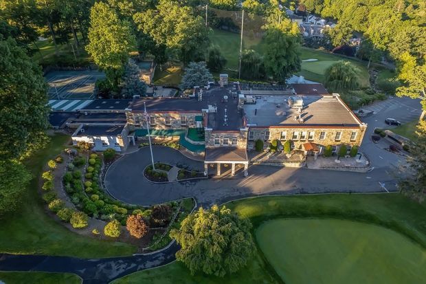Aerial view of a stately stone building with green awnings, gardens, and a golf course.