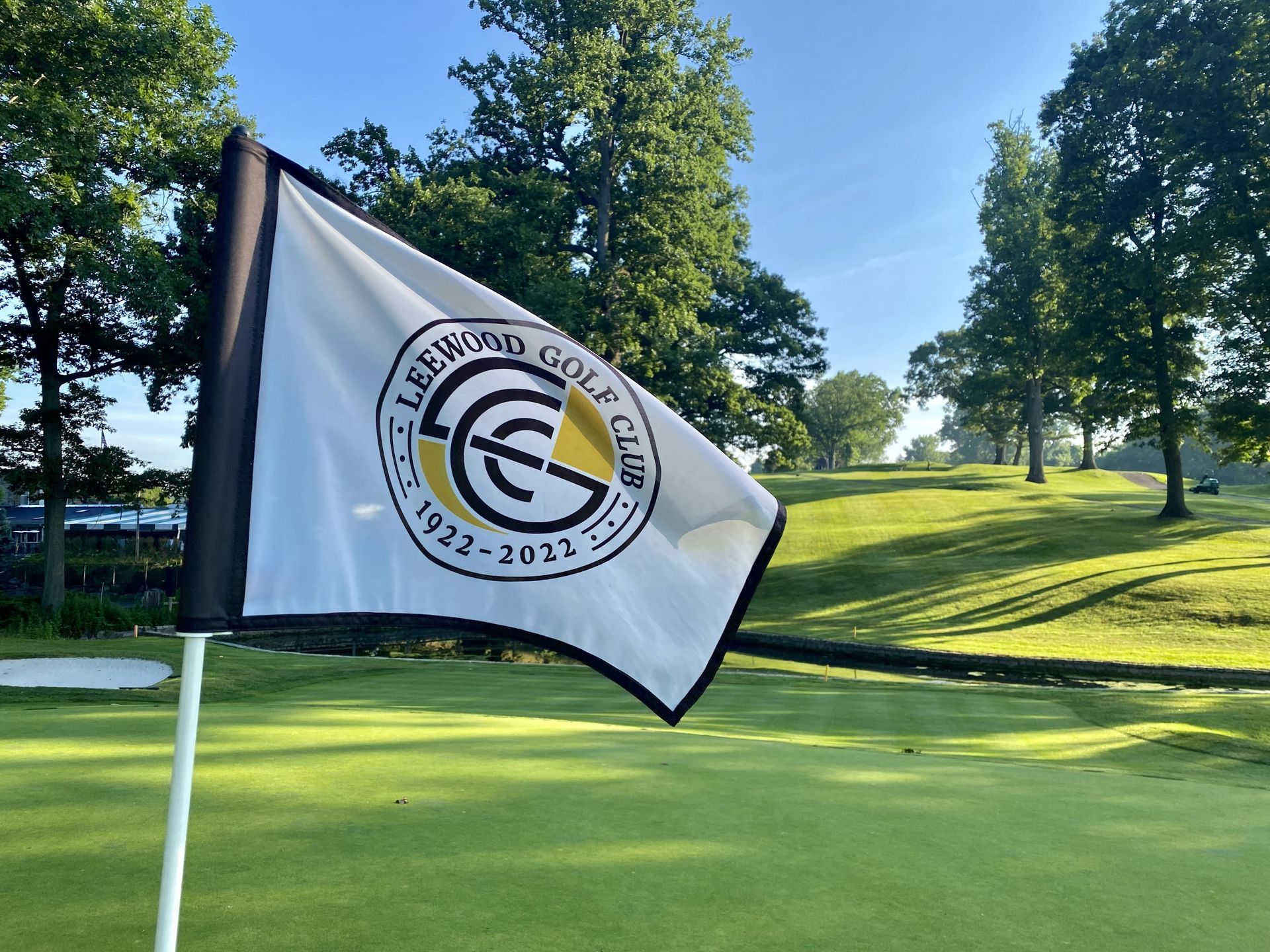 A flag with the Leewood Golf Club logo flying on a green, sunny golf course.