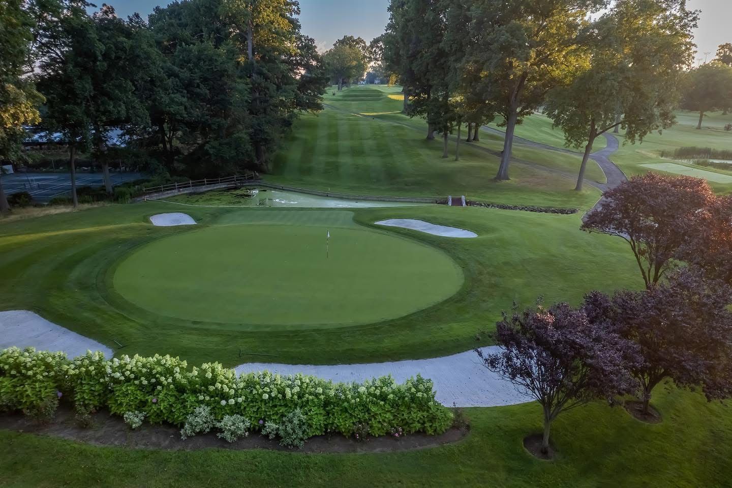 Green golf course with sand traps, trees, and flag in the center.