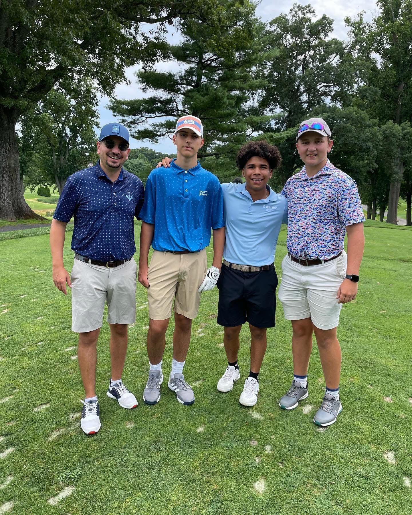 Four people in golf attire pose on a green field.