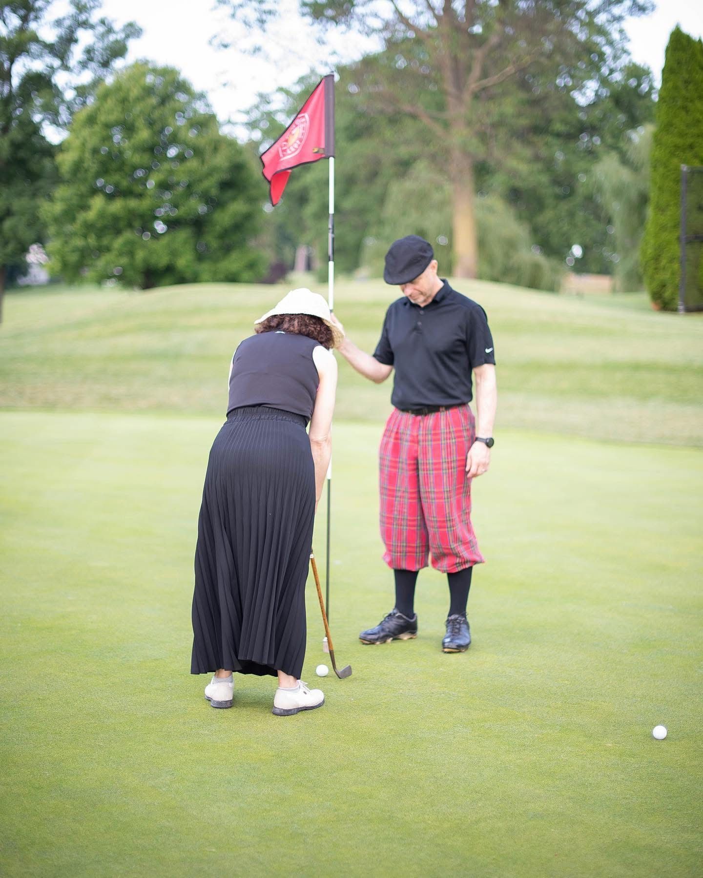 Woman putting a golf ball while a man looks on, standing near the flag on a green golf course.