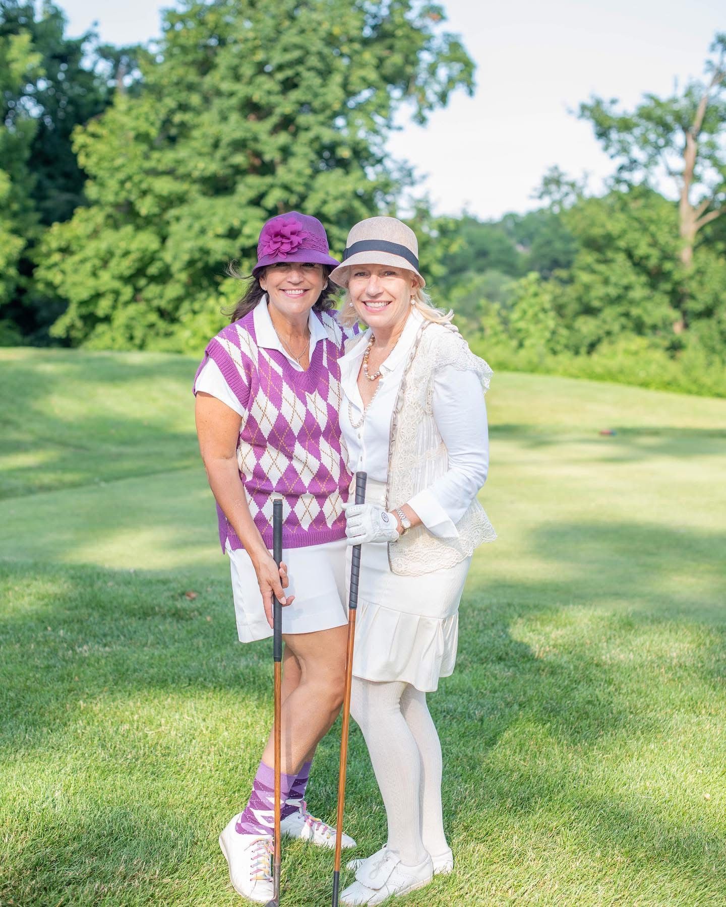 Two women in vintage golf attire posing on a golf course, smiling.