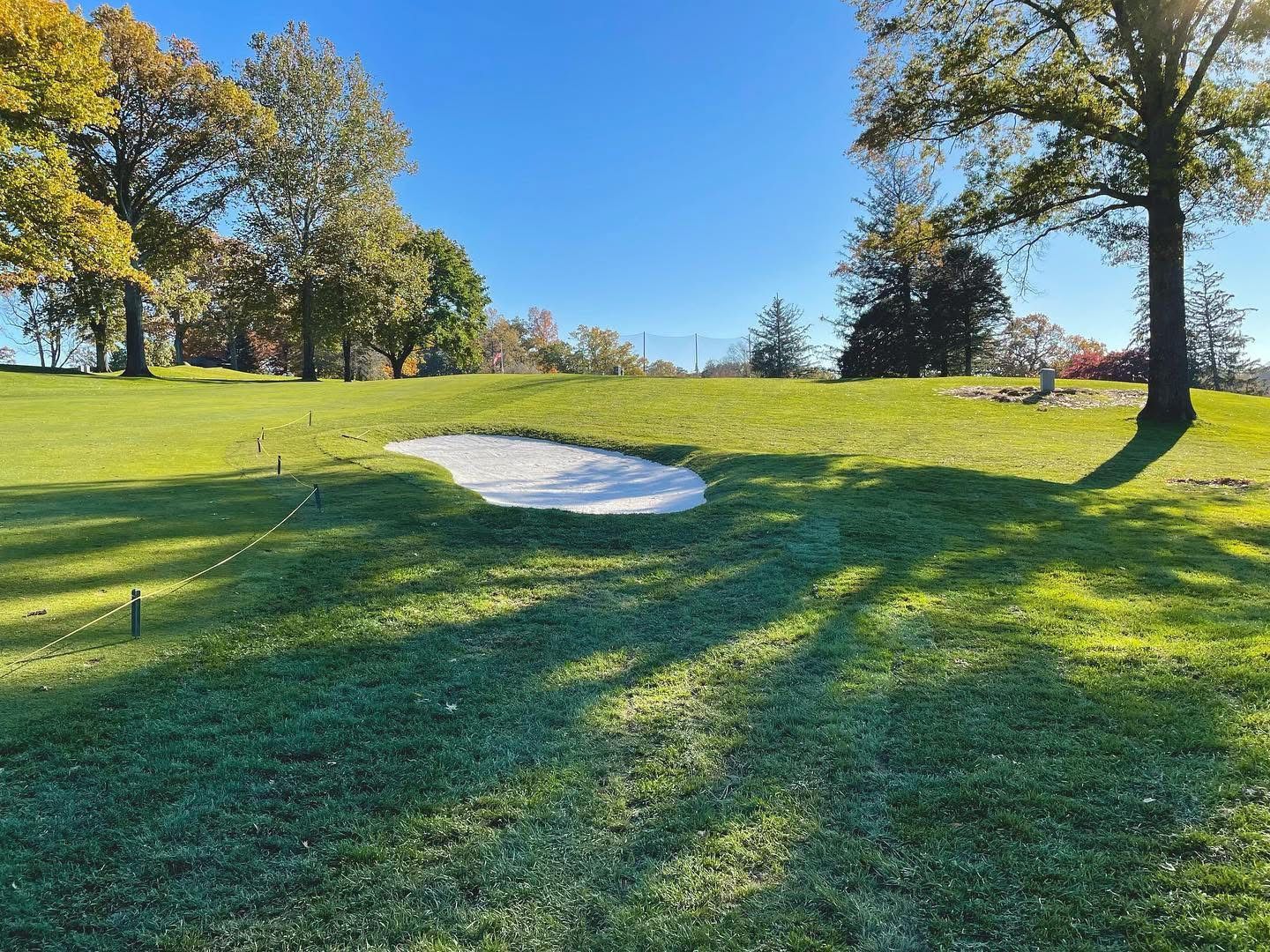 Golf course with a sand trap, green grass, and trees under a clear blue sky.