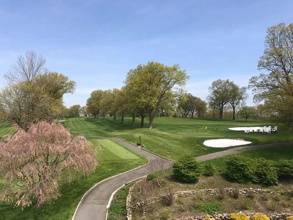 Golf course with winding path, green grass, trees, and sand traps under a blue sky.