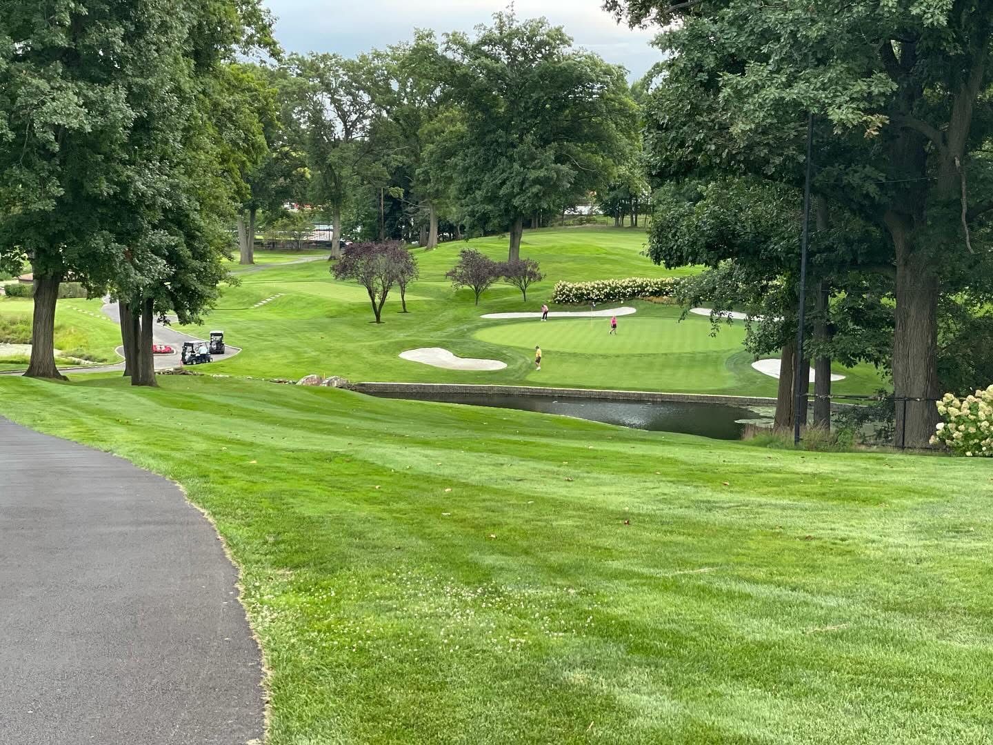 Green golf course with a pond, sand trap, and trees.