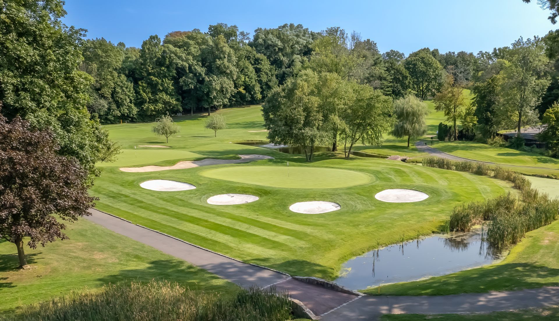 Golf course with green grass, sand traps, small pond, and trees under a blue sky.