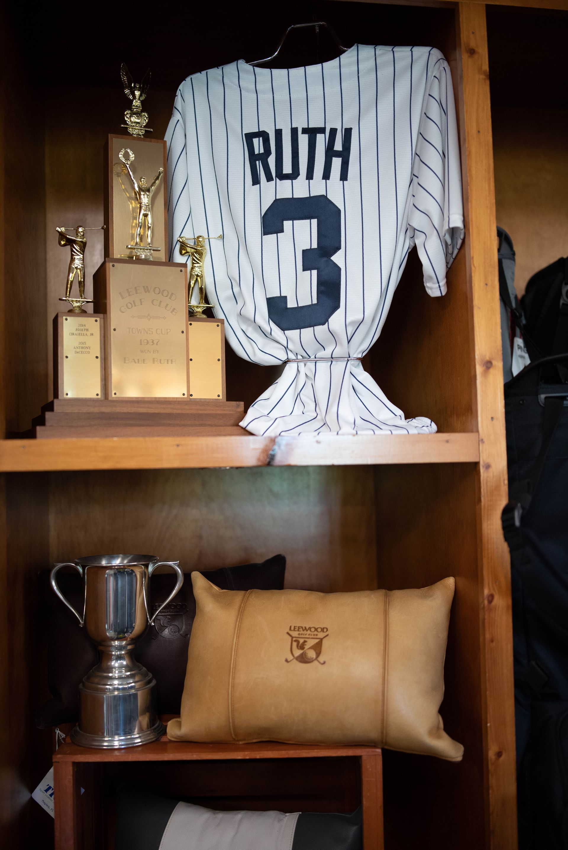 Shelf with Babe Ruth jersey, trophies, silver cup, and a leather pillow.