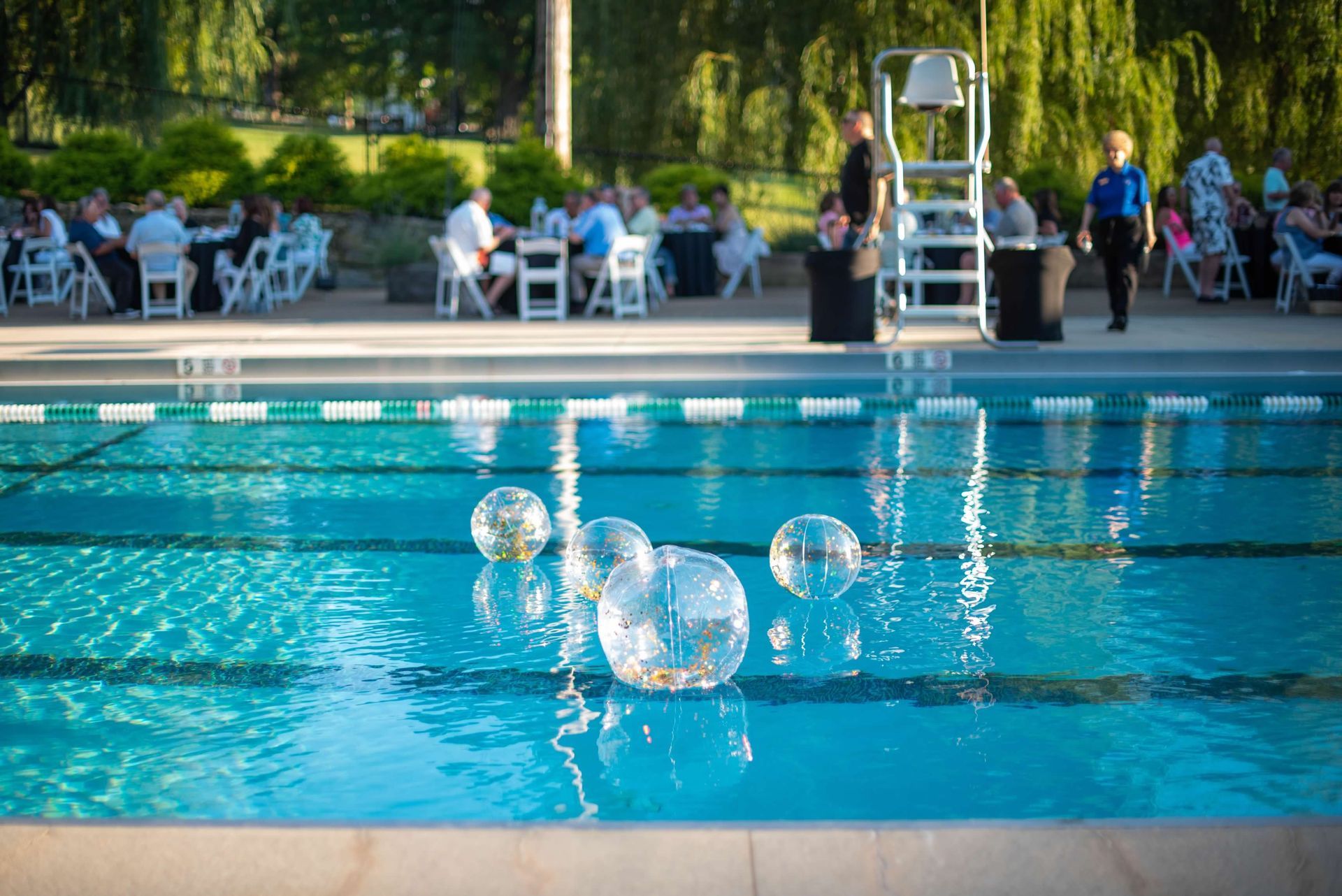 Swimming pool with floating orbs; outdoor event with tables and people in background.