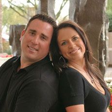 A man and a woman are standing back to back and smiling for the camera.