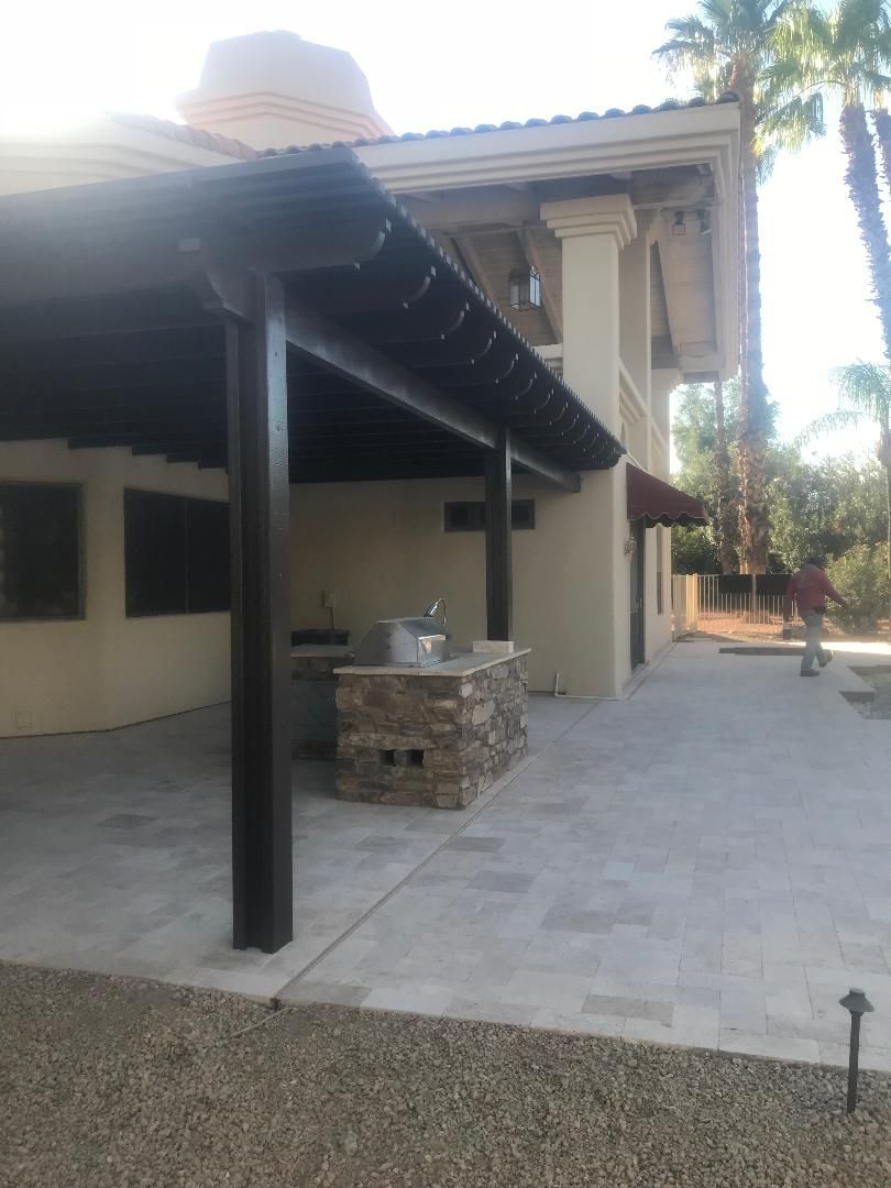 A man is walking in front of a house with a covered patio.