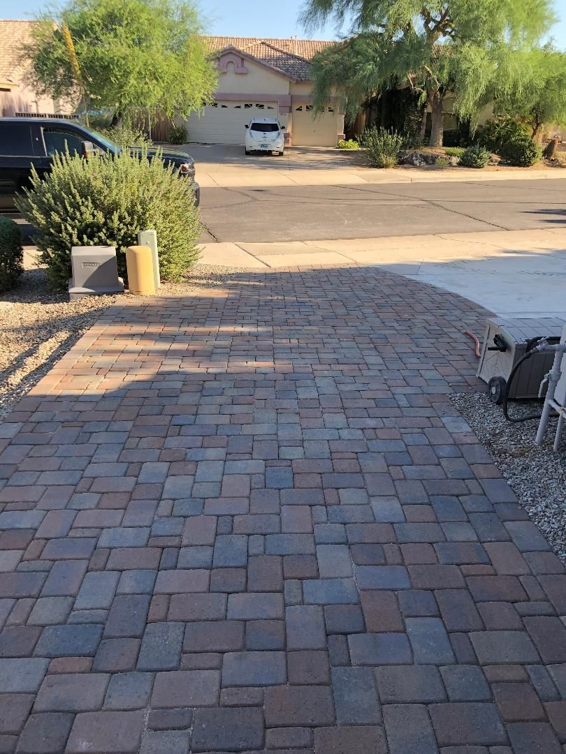 A brick driveway in front of a house with a car parked in the driveway.