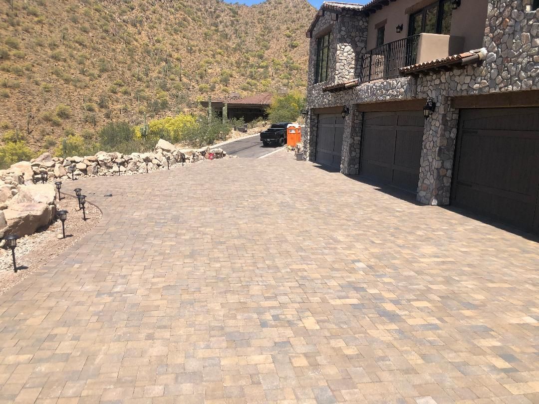 A brick driveway leading to a house with a mountain in the background.