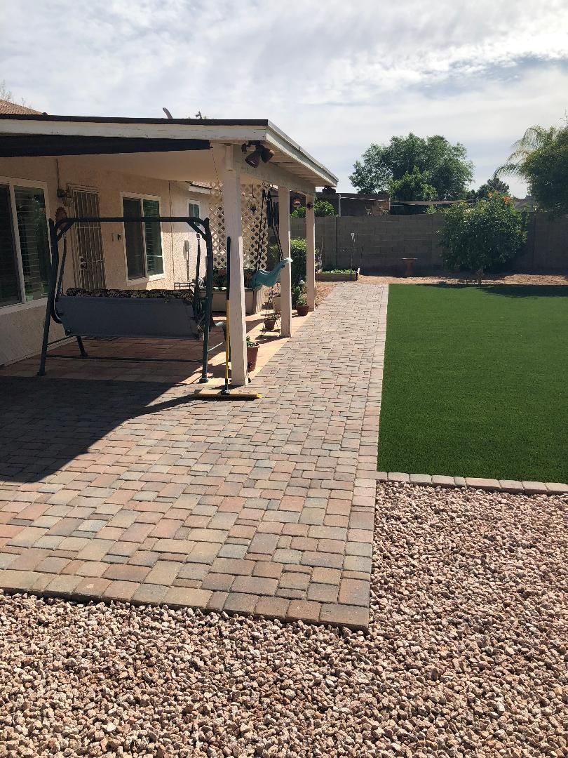 A brick walkway leading to a house with a swing in the backyard.