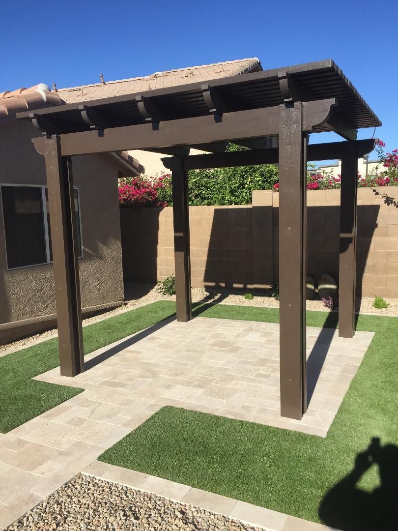 A pergola is sitting on top of a lush green lawn in front of a house.