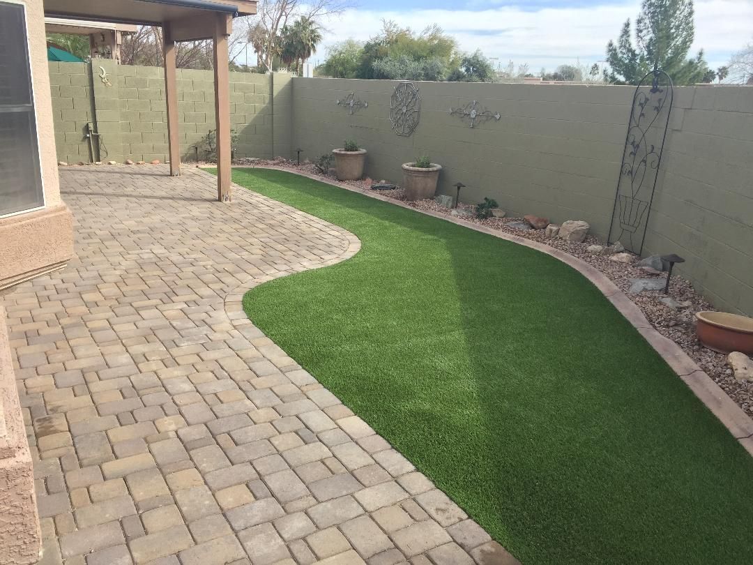 A backyard with a brick walkway and a lush green lawn.