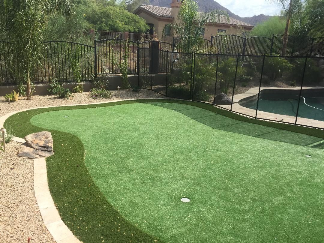 There is a putting green in the backyard next to a pool.