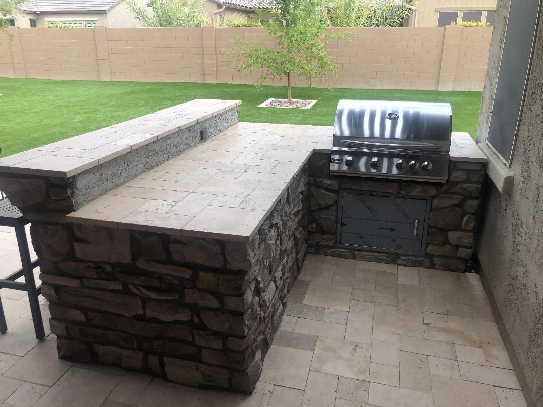 A grill is sitting on top of a stone counter on a patio.