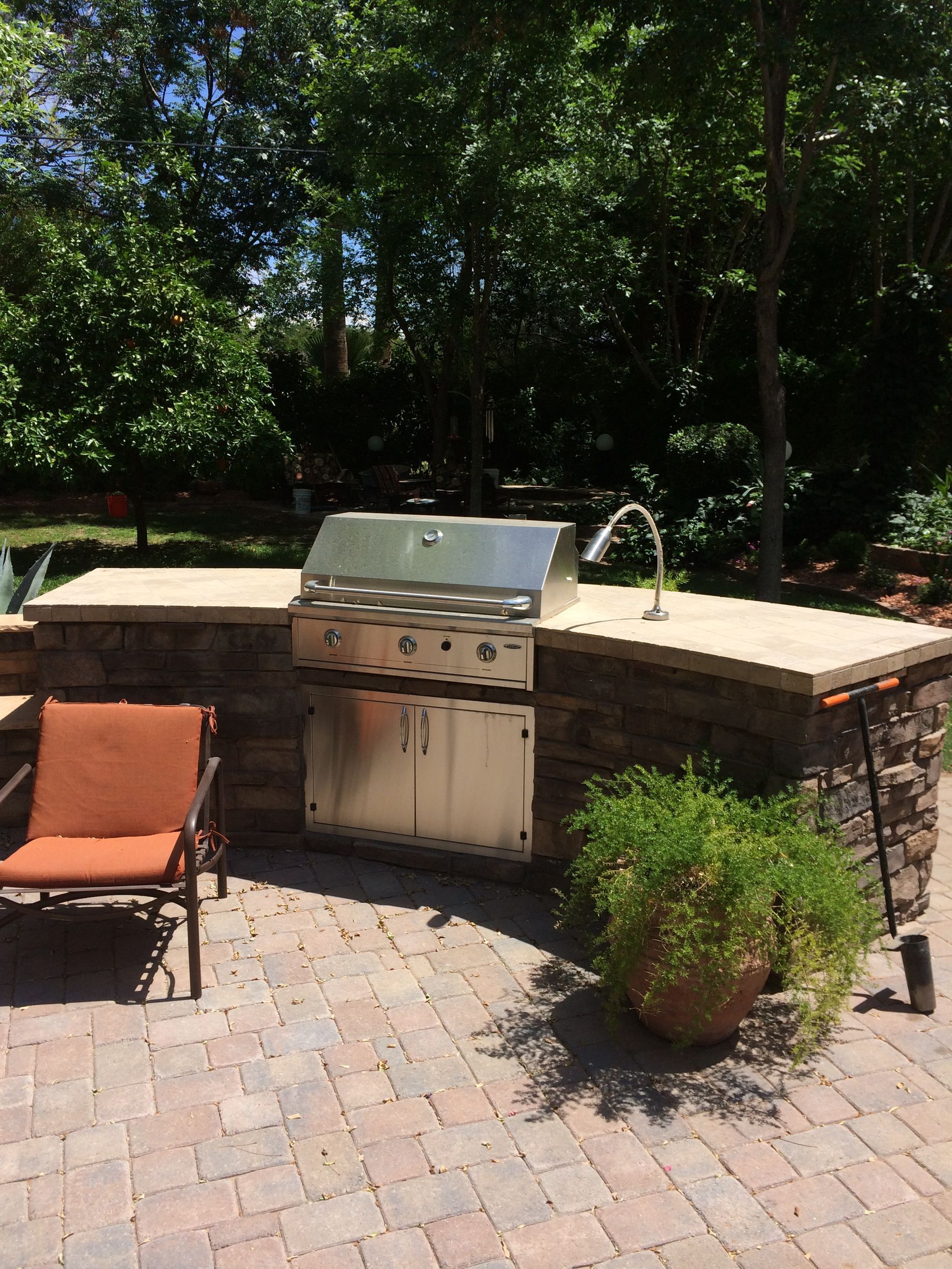 A grill is sitting on a brick patio next to a chair.