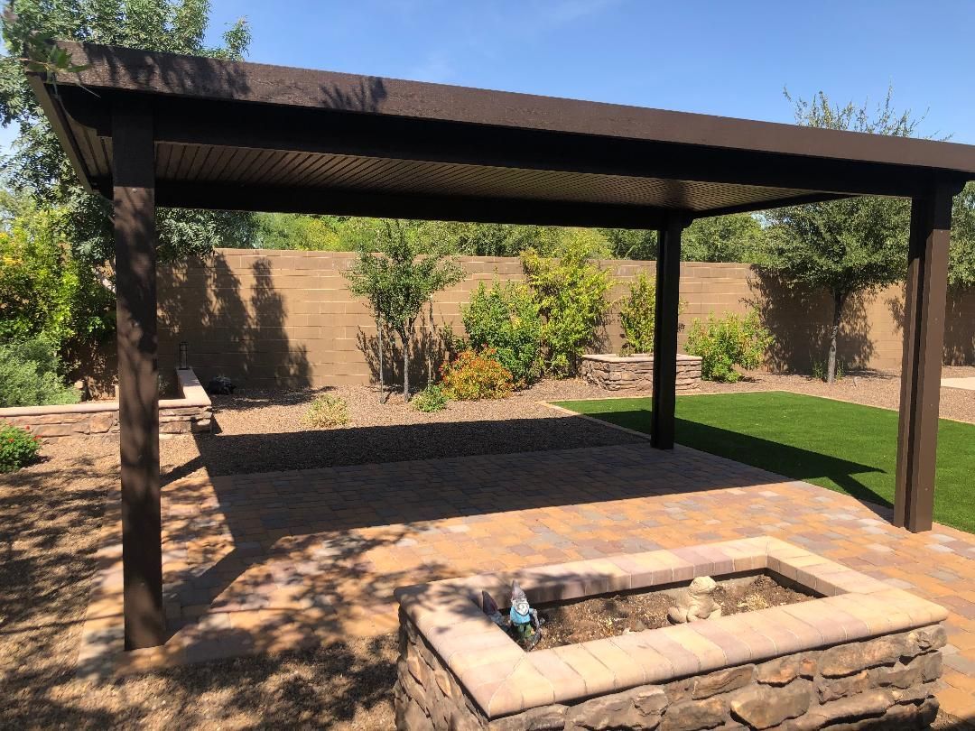 There is a fire pit under a pergola in the backyard.
