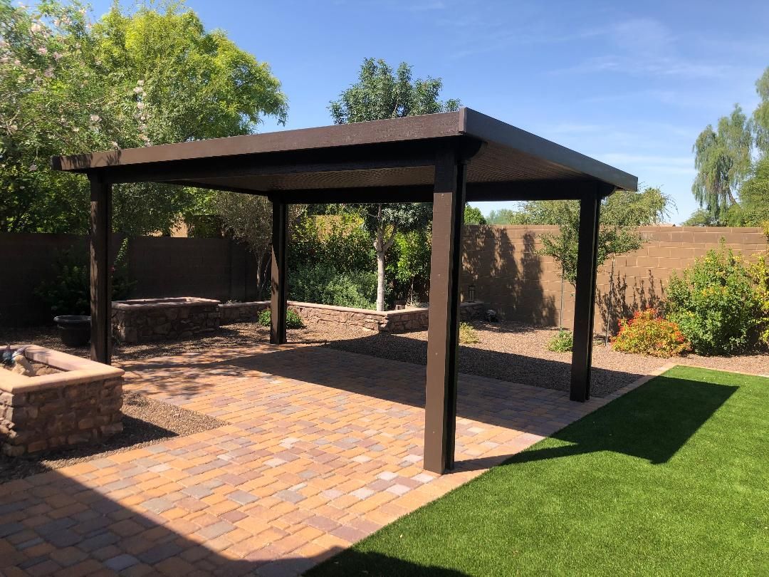 A pergola is sitting on top of a brick patio in a backyard.