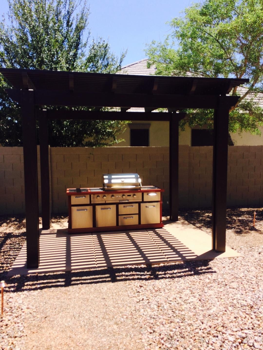 An outdoor kitchen with a grill under a pergola