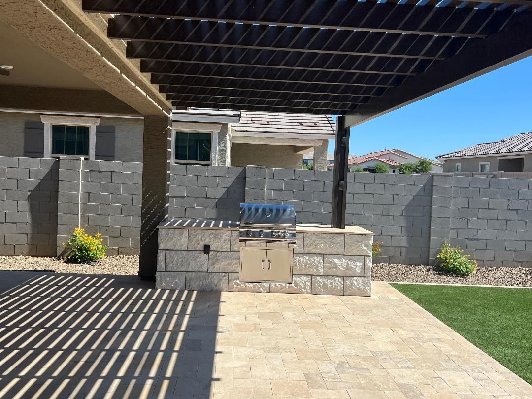 A patio with a grill under a pergola and a brick wall