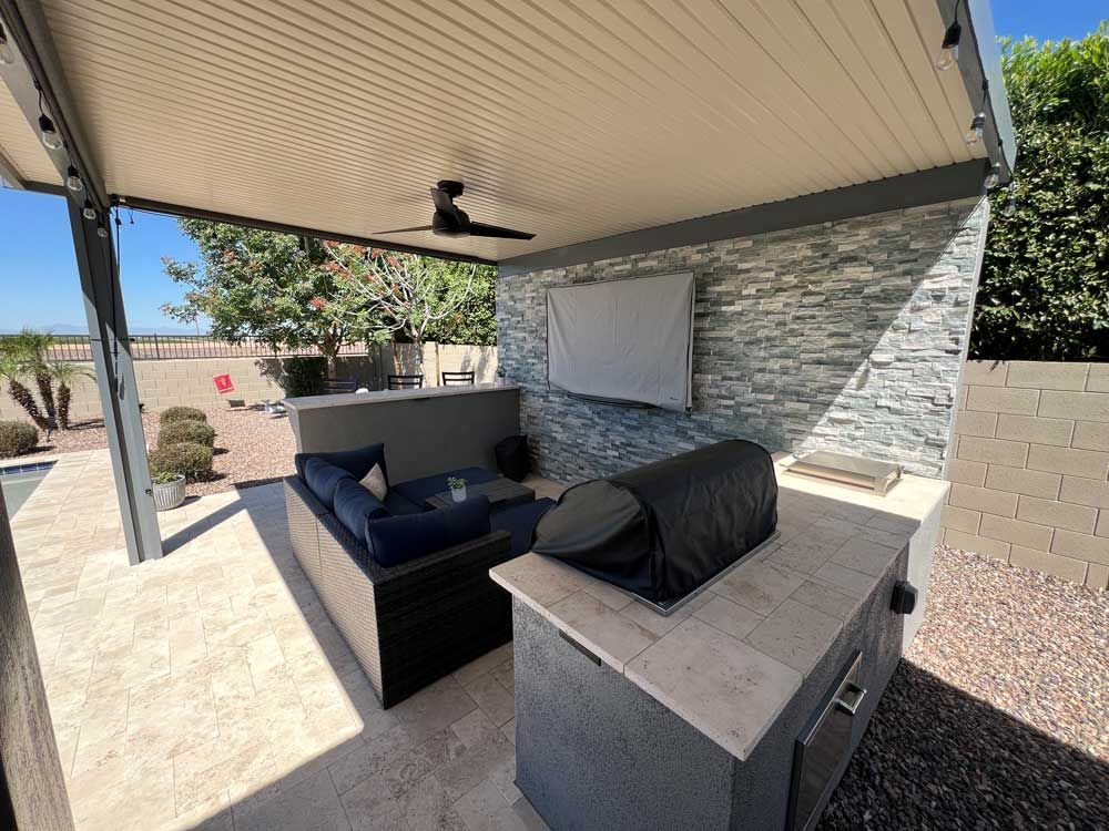 A patio with a couch, grill, television and ceiling fan.