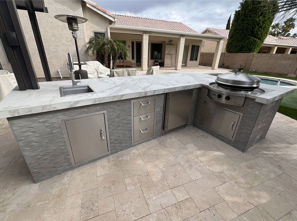 A large outdoor kitchen with a grill and sink in front of a house.
