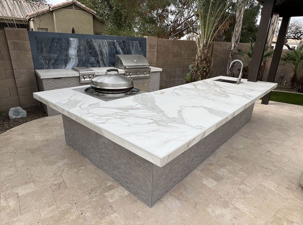 An outdoor kitchen with a marble counter top and a grill.