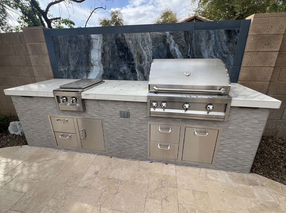 An outdoor kitchen with a grill and a waterfall in the background.