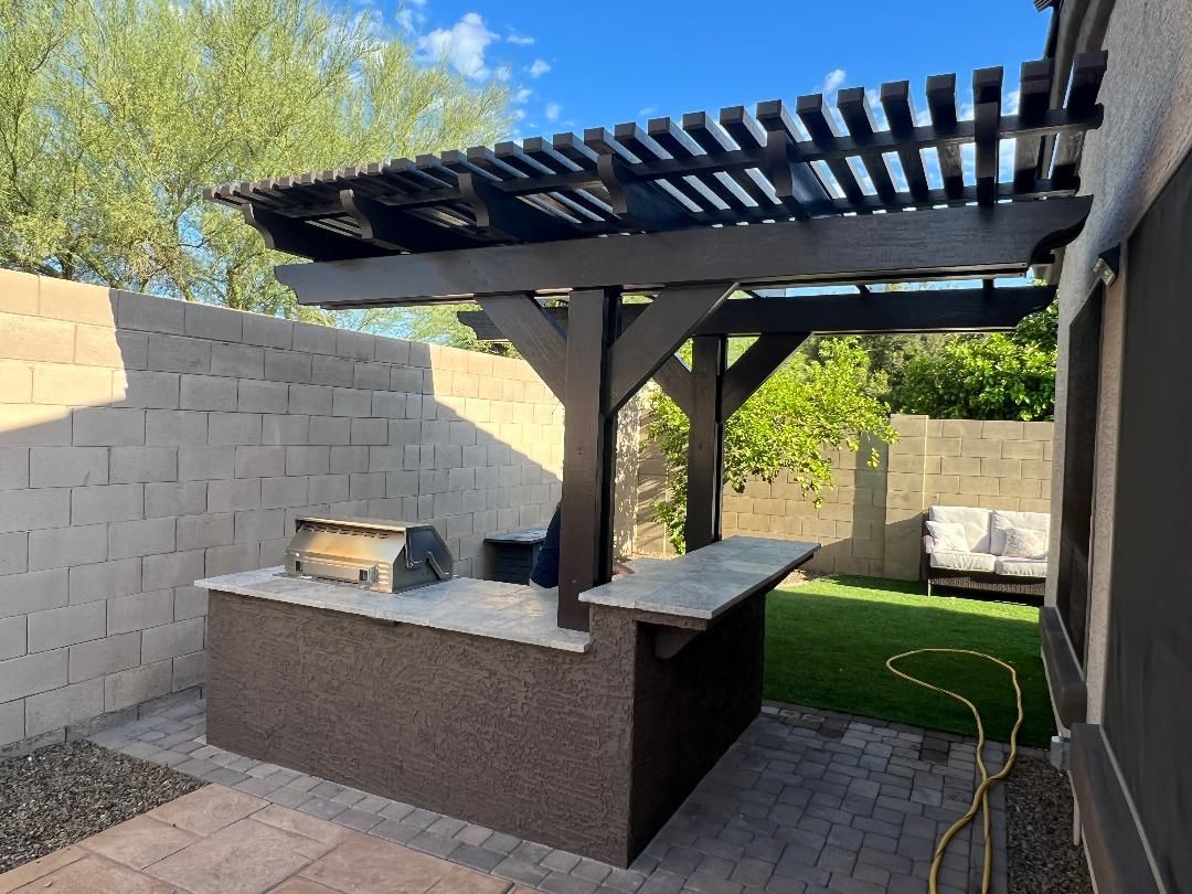 A patio with a grill and a pergola over it