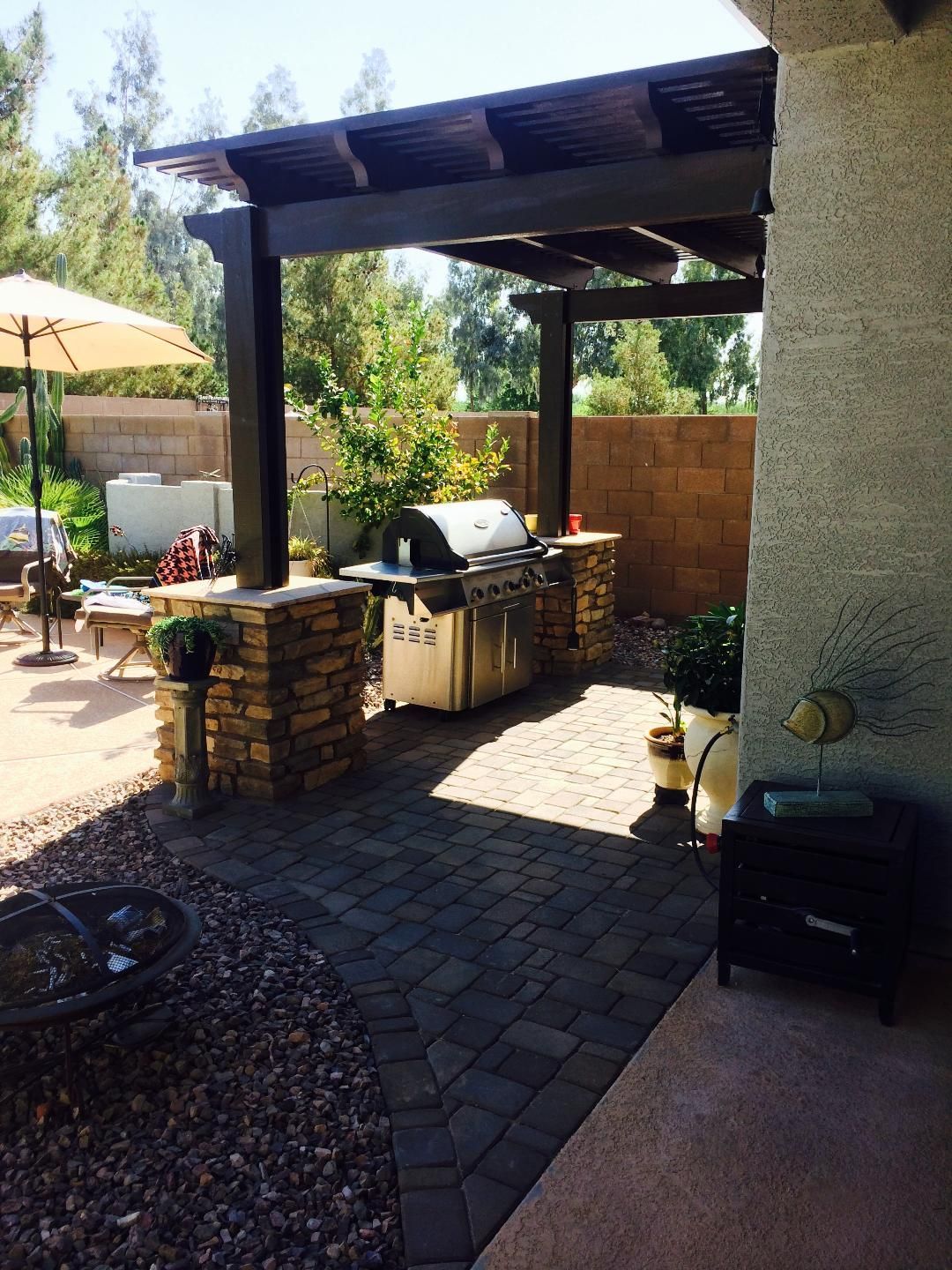 A patio with a grill under a pergola and umbrellas