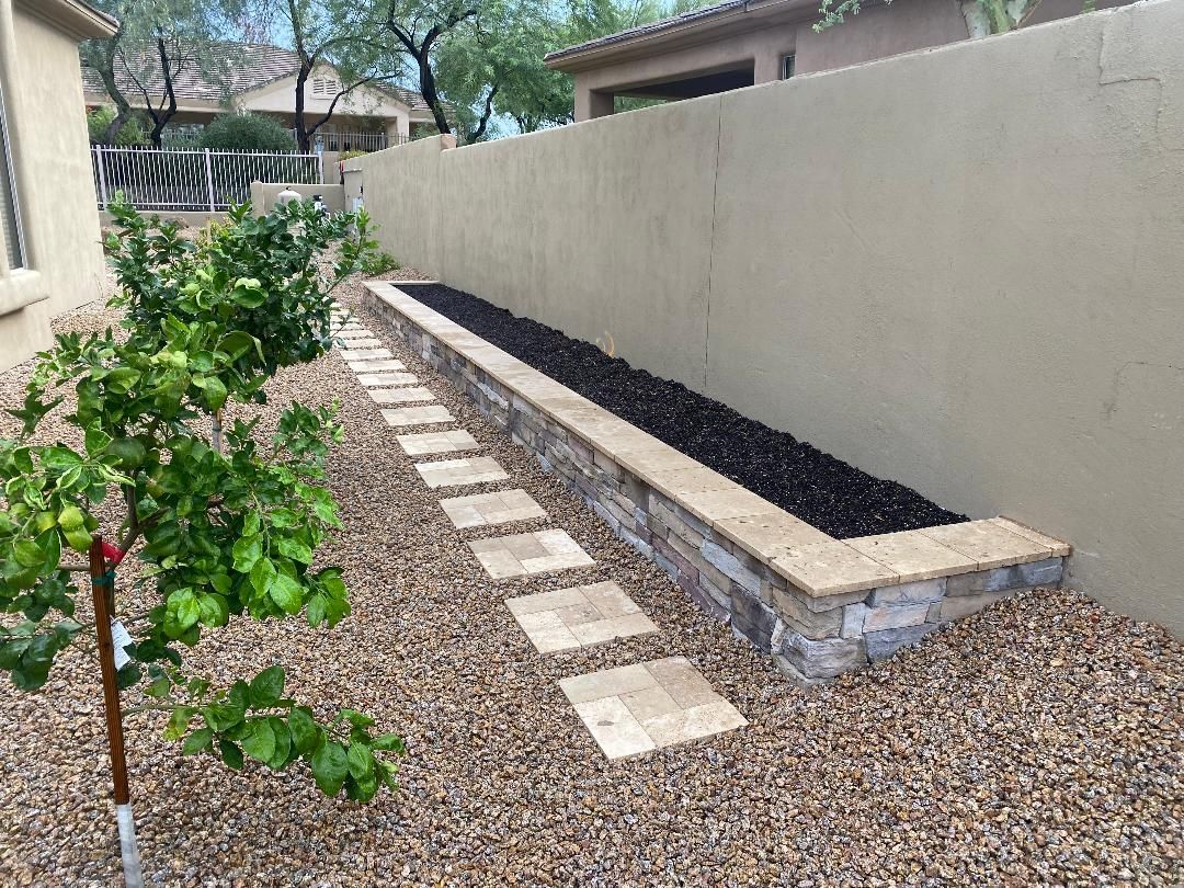 A stone walkway leading to a planter in a garden next to a house.