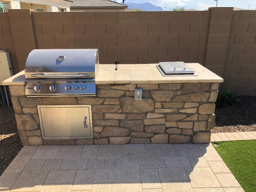 A grill is built into a stone wall in a backyard.