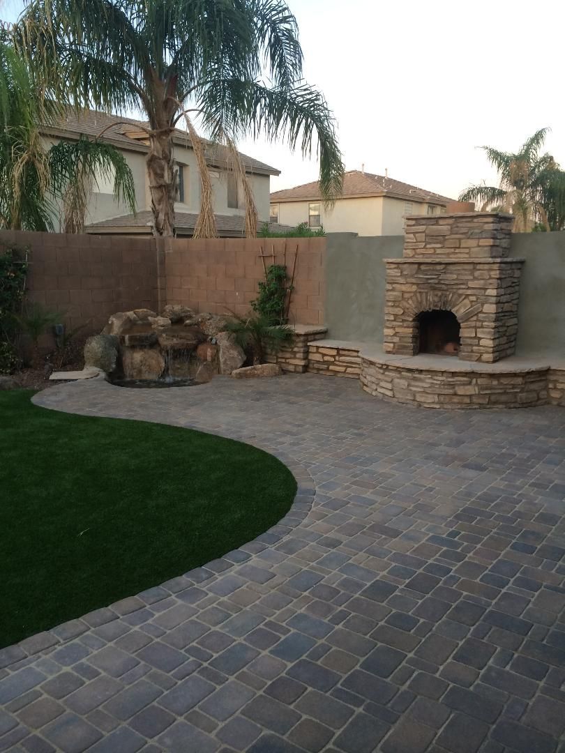 A patio with a fireplace and a waterfall in the backyard.