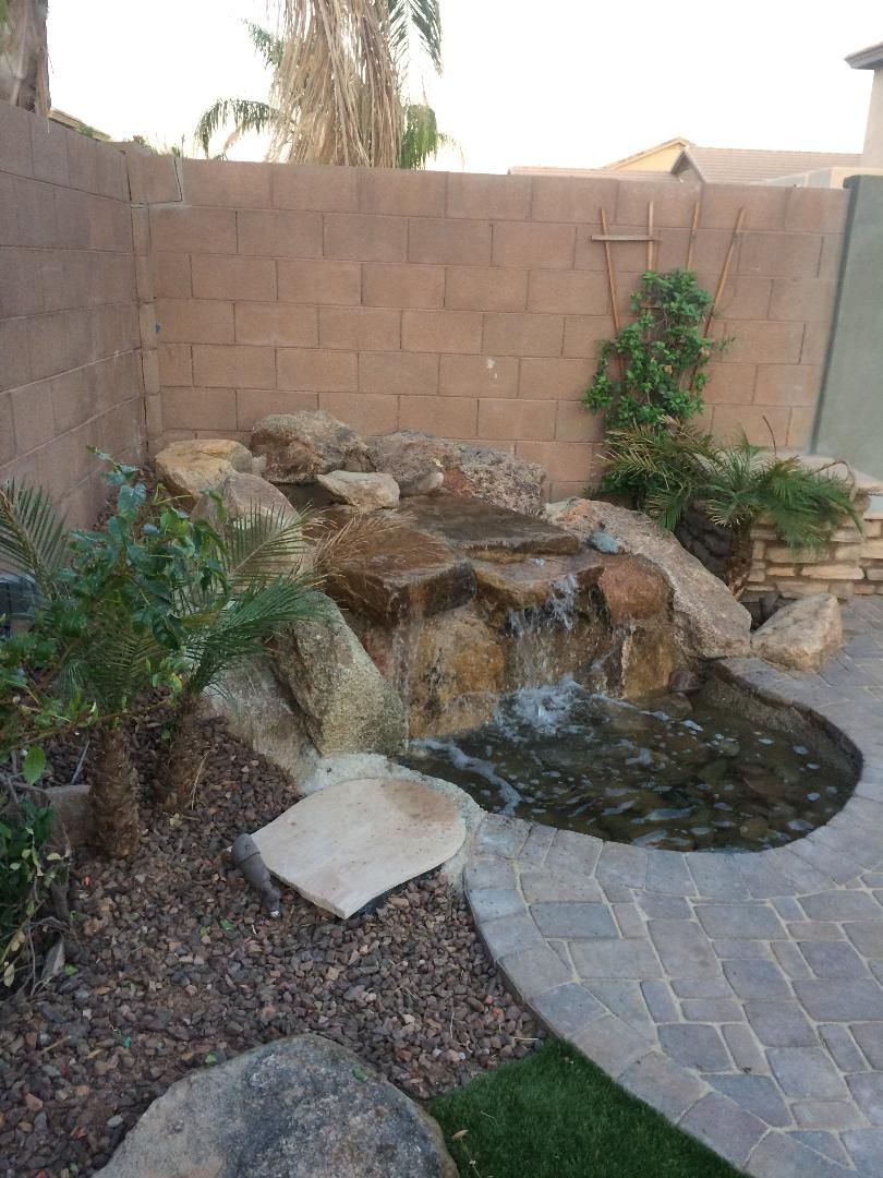 A waterfall is surrounded by rocks and plants in a backyard.