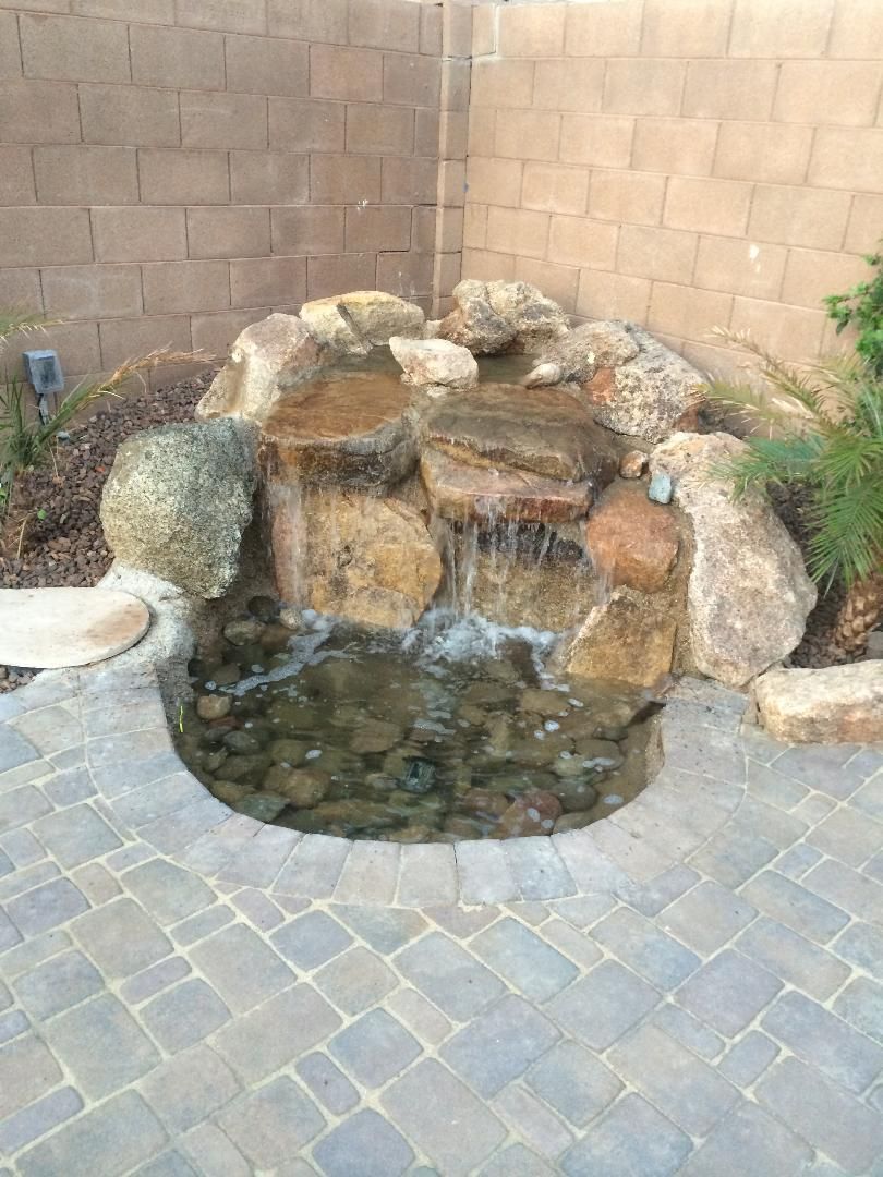 A small waterfall is surrounded by rocks on a brick patio.
