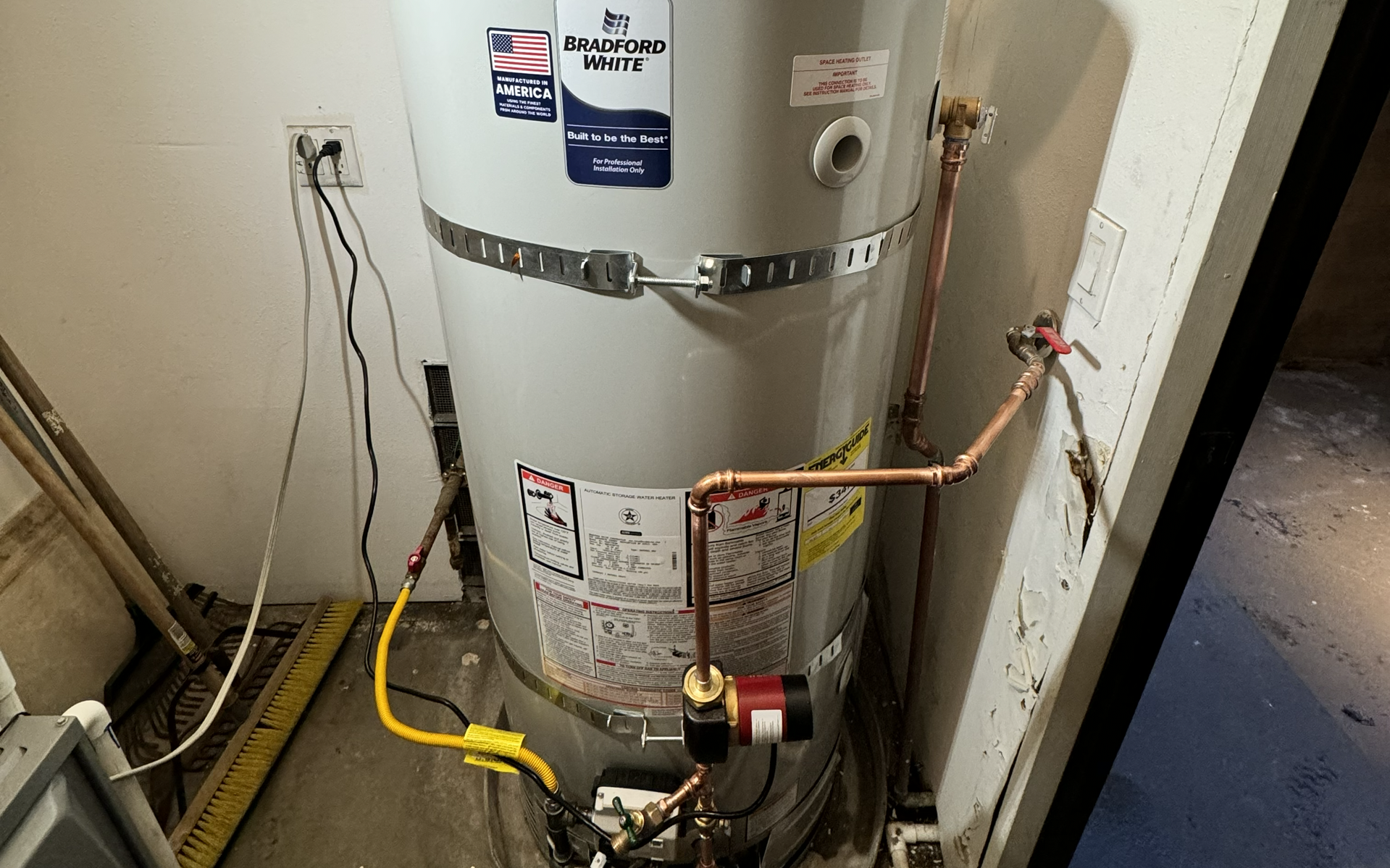 Water heater in a utility closet with exposed wires and yellow gas line attached.
