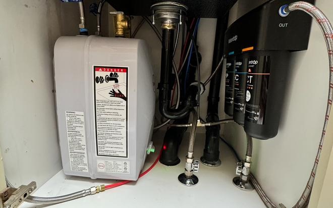 Under-sink plumbing with water heater, pipes, and black filtration unit in a cabinet