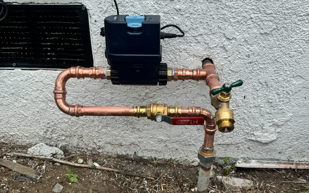 Outdoor copper pipes with a black water meter and shutoff valves against a stucco wall