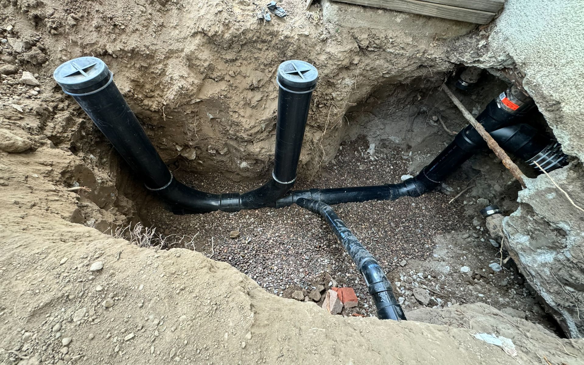 Underground plumbing pipes and vents installed in a dirt trench at a construction site